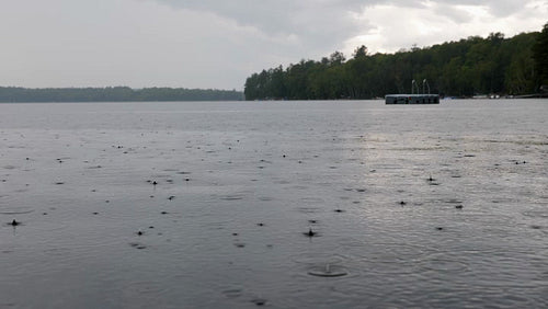 Rain falls on surface of lake. Swimming dock in distance. Cottage country. 4K.