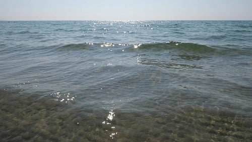 Slow motion sunlit lake with crashing wave. Rippled sand visible below. HD video.