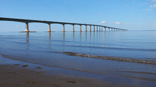 Confederation bridge with lapping water on the beach. New Brunswick, Canada. 4K.