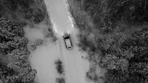 Tracking birdseye drone shot of SUV on snow covered rural road. Evening. Black and white. 4K.