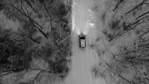 Tracking birdseye drone shot of SUV on snow covered rural road. Evening. Black and white. 4K.