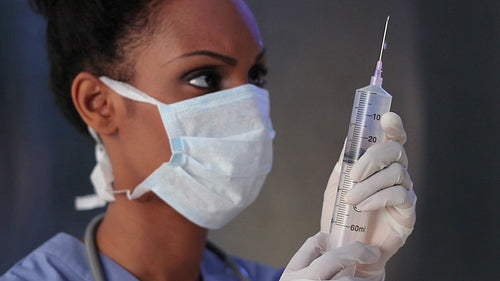 Young black female nurse with mask holds up giant needle. HD.