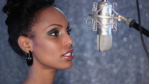 Attractive young black woman sings into studio microphone. HD.