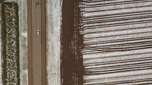 Drone following road beside farmers field. Car passes. Winter in Ontario, Canada. 4K.