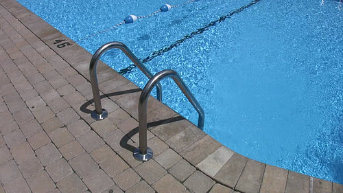 Swimming pool detail. Side of pool showing metal handles of pool ladder. HD.