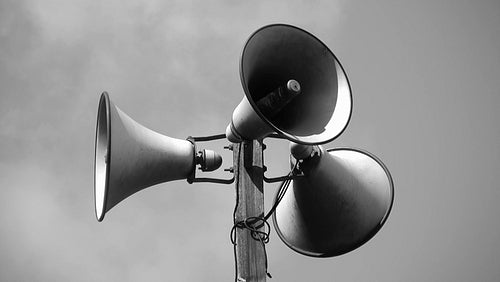 Megaphone tower with three speakers. Black and white. Clouds in background. HDV footage. HD.