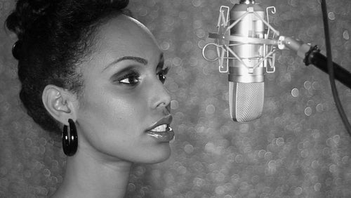 Attractive young black woman sings into studio microphone. Black and white. HD.