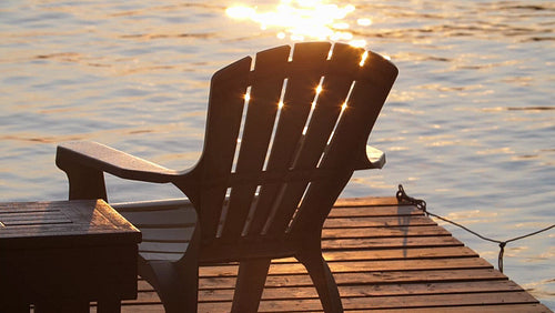 Slow motion golden sparkles from lake with dock and Muskoka chair. HD.