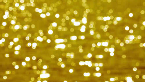 Defocused glittering highlights on sunlit summer lake water. Gold tint. 4K.