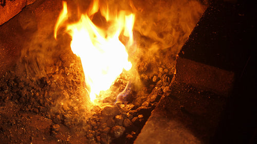 Blacksmithing forge. Using a rake to pull coal and charcoal into the fire. 4K.